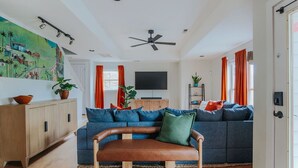 Een woonkamer met een blauwe bank, een bruine leren zitbank, een houten kast en een televisie op een dressoir.