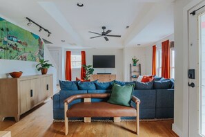 Een woonkamer met een blauwe bank, een bruine leren zitbank, een houten kast en een televisie op een dressoir.