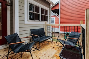 A wooden deck with three black metal chairs and a wooden table.