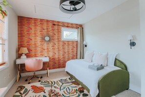A bedroom with a bed, a desk, a chair, a window, and a wall with a striped pattern.