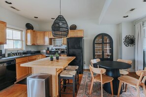 Une cuisine moderne avec des meubles en bois, un îlot central, un réfrigérateur noir et un coin repas comprenant une table ronde et des chaises.