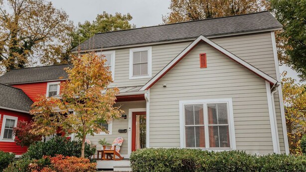 A two-story house with a front porch, a red door, and a small garden with a tree and shrubs. - Oasis on 5th: walk to downtown Cville & UVA (Charlottesville,)