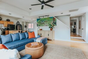 Un salon moderne avec un canapé bleu, une table basse en bois et un grand tableau au-dessus de la cheminée.