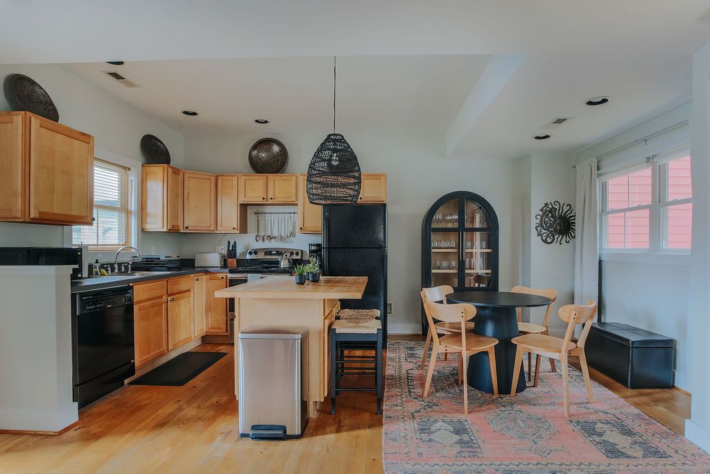 A modern kitchen with wooden cabinets, a central island, and a dining area with chairs.