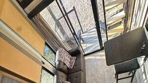 A compact kitchen with a built-in oven, a microwave, and a coffee machine. There is a window above the sink, and a small seating area with a cushion. - Buffalo Drift Tiny Home (Interior)