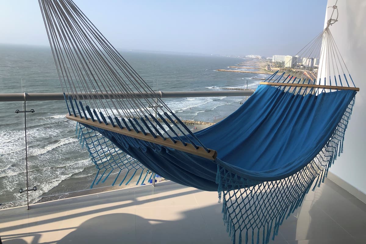 A hammock chair with a view of the ocean and a cityscape in the background.