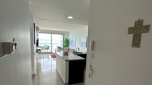 A modern kitchen with a central island, a dining area with chairs, and a large window providing a view. - Alta Mar - Bella Cartagena Apartments (Cartagena)