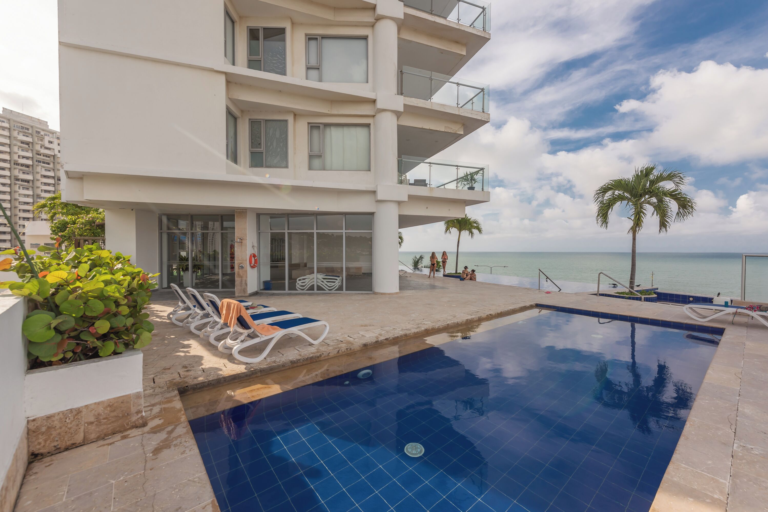 A modern hotel with a pool, outdoor seating, and a view of the ocean.