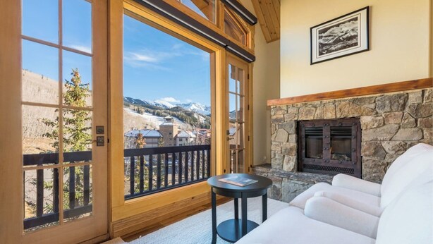 A cozy room with a stone fireplace, a sofa, and a view of mountains through large windows. - Beautiful 3 BDR Telluride Escape Close to Skiing with Private Hot Tub (Mountain Village)