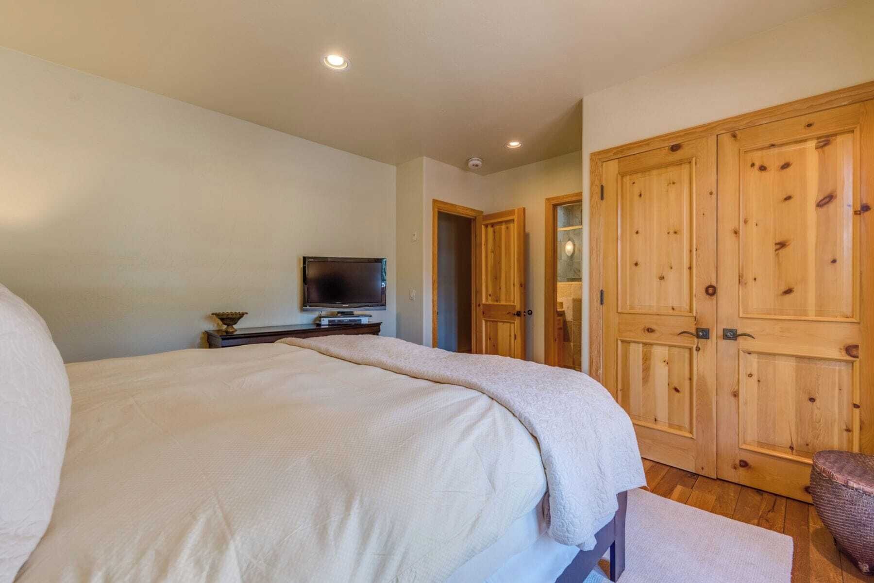A bedroom with a large bed, a television on a stand, wooden wardrobes, and a small chair.