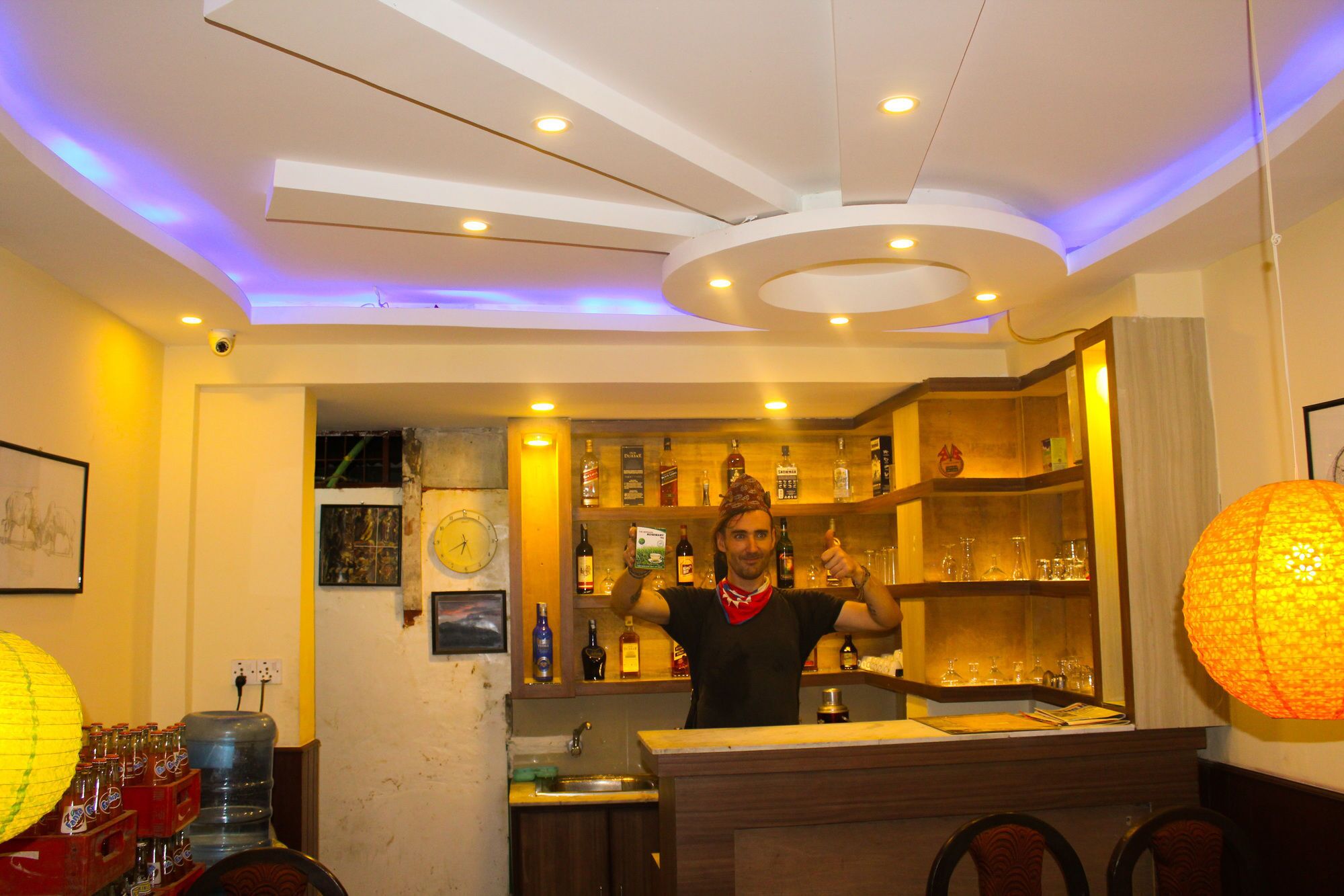 A bar area with a counter, shelves of bottles, and a clock on the wall.