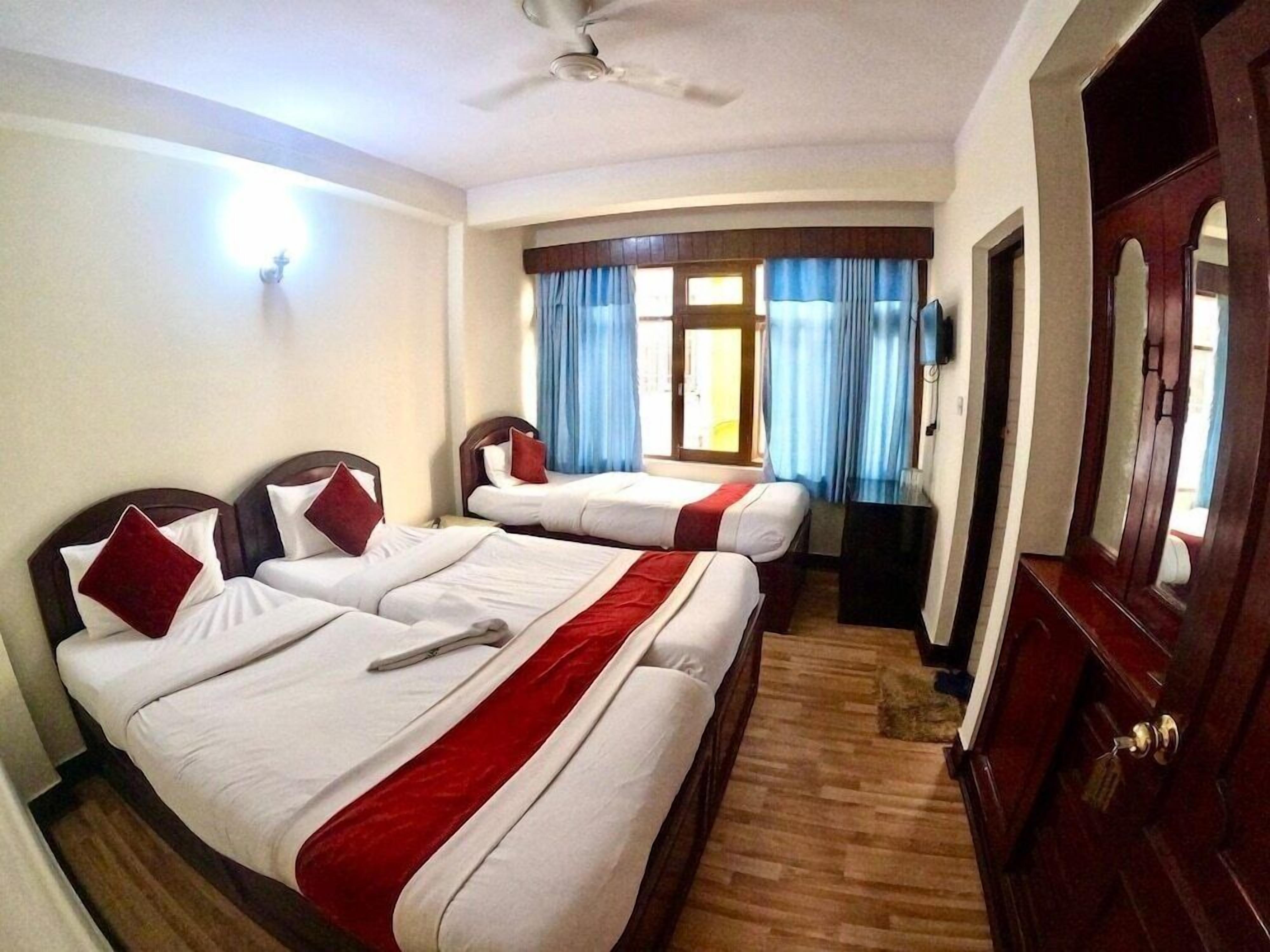 A hotel room with two beds, a ceiling fan, a wooden floor, and a large mirror.