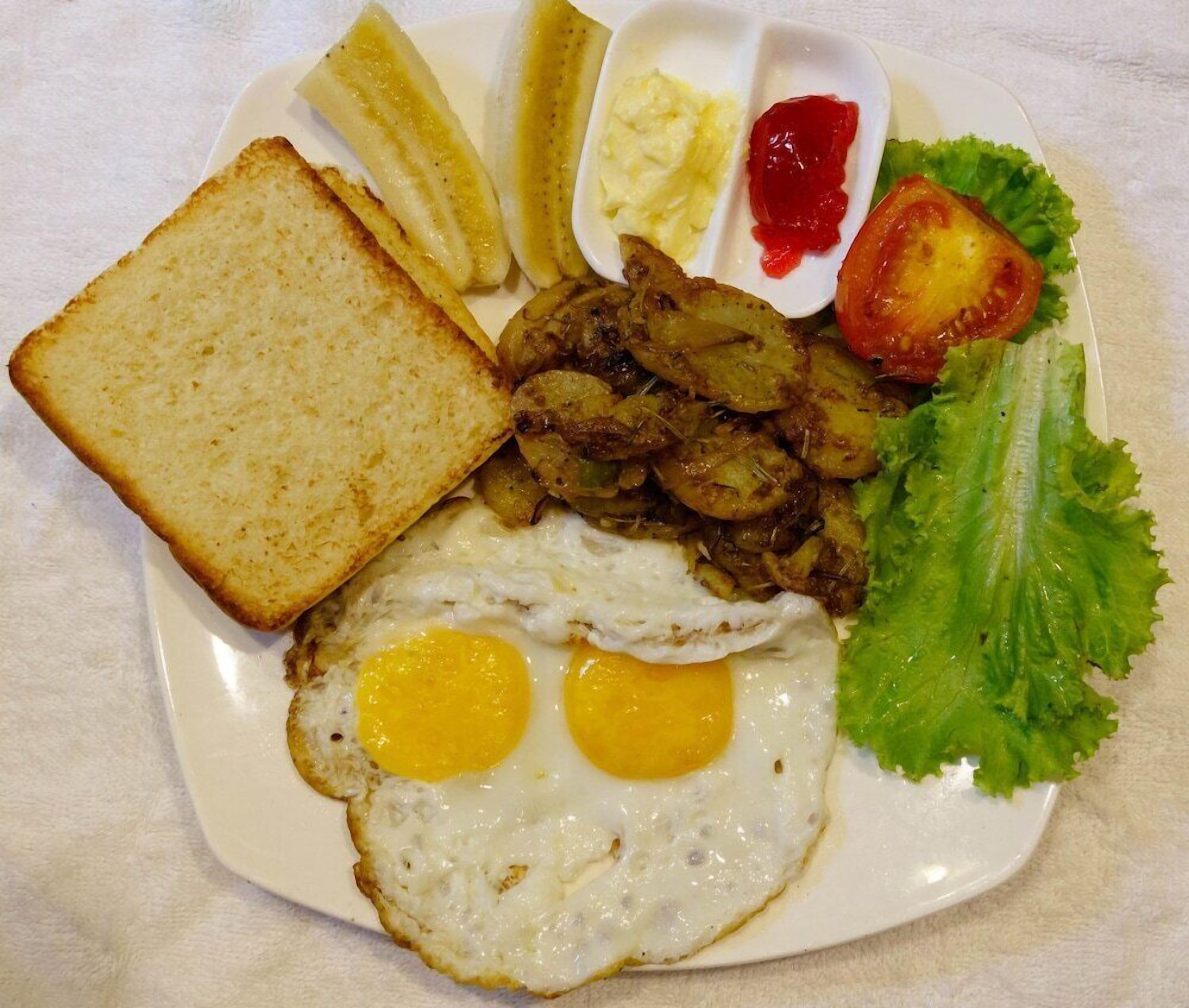 En tallerken med morgenmad, herunder æg, ristet brød, kartofler og en skive tomat.