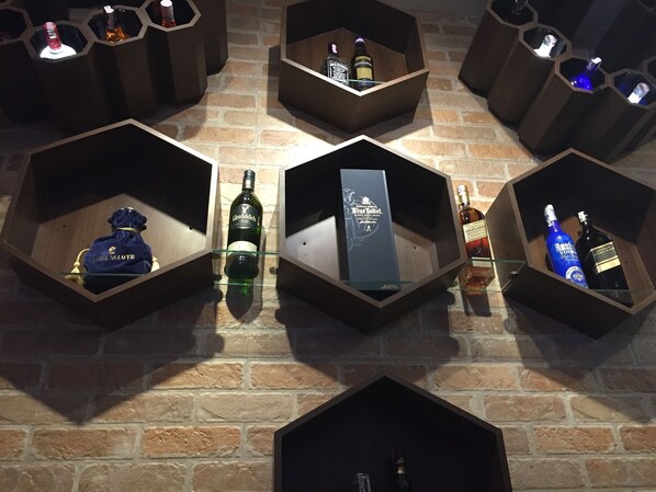 Una exhibición hexagonal de botellas variadas y una caja sobre un muro de ladrillo.