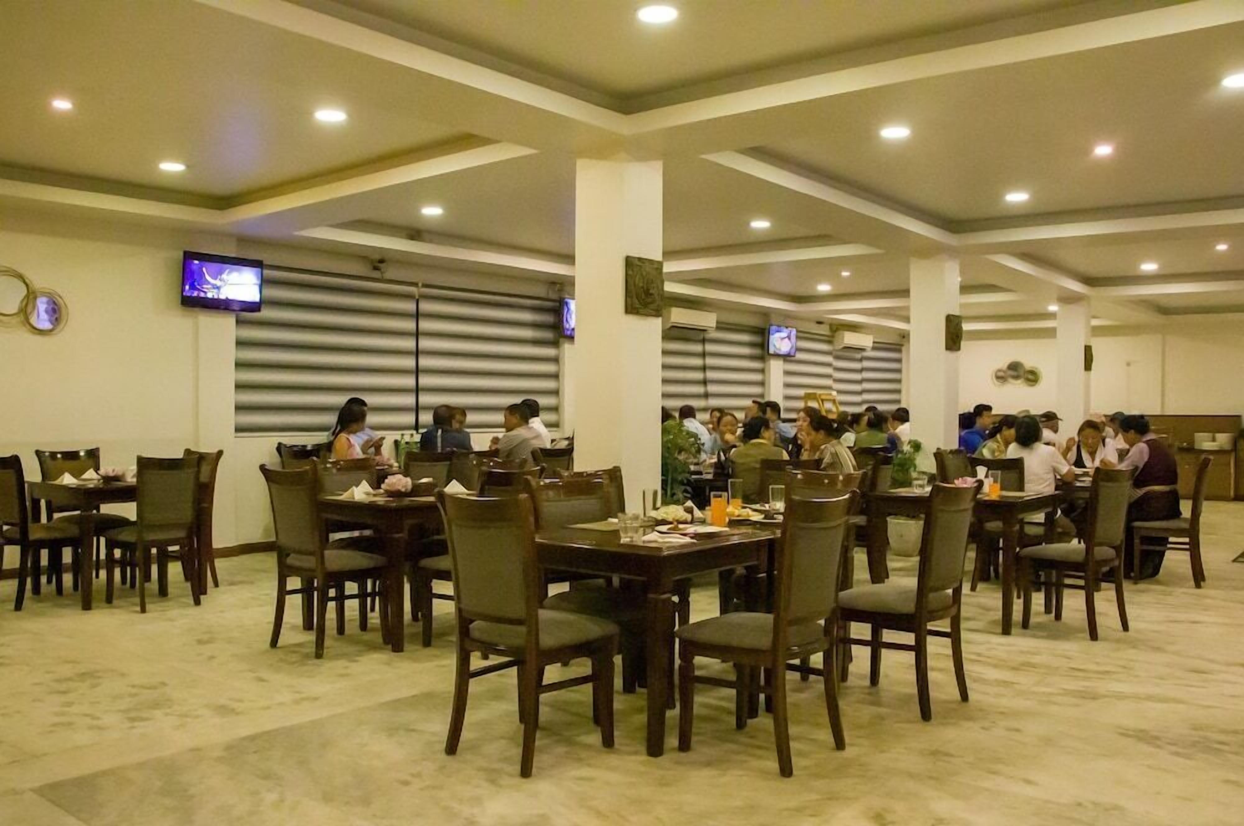 Un grand espace dédié à la salle à manger, avec plusieurs tables et chaises, des luminaires au plafond et des téléviseurs fixés au mur.