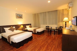 A hotel room with two beds, a desk, chairs, and a large window with curtains.