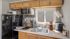 Eine Küche mit Holzausstattung, einem schwarzen Kühlschrank, einer Mikrowelle, einer Kaffeemaschine und einem Fenster mit Aussicht.