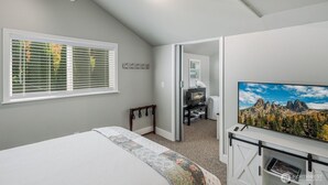 Ein Schlafzimmer mit einem Bett, einem Fernseher auf einem Schrank, einem Fenster mit Jalousien und einer Tür zu einem anderen Raum.