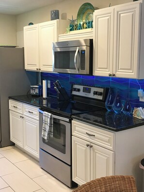 Eine Küche mit weißen Schränken, einer Mikrowelle, einem Backofen und einer Spritzschutzwand mit blauen Wellenmustern.