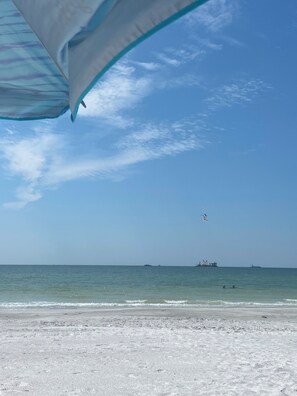 Ein Strand mit blauem Himmel, ruhiger See und Schiffen in der Ferne.