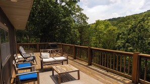 Une terrasse en bois, aménagée avec du mobilier d’extérieur, notamment des chaises longues et un canapé, donnant sur une zone boisée.