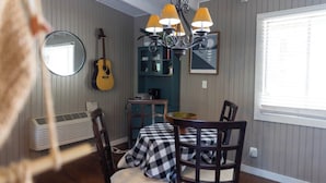 Un coin repas avec une nappe à carreaux, des chaises en bois, une guitare et un lustre.
