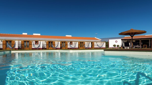 Une piscine à l’eau d’un bleu cristallin, un bâtiment doté d’un toit en tuiles et un espace de repos abrité.