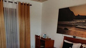 Une chambre d’hôtel avec un grand lit, une table de chevet en bois, une chaise et un tableau représentant une scène de plage.