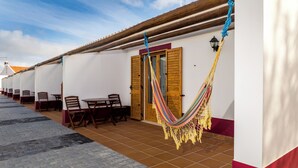 Une rangée de bâtiments blancs avec des portes et des fenêtres en bois, une terrasse carrelée et un hamac suspendu au toit.