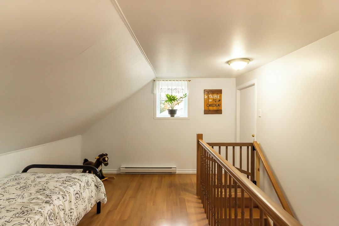 A bedroom with a bed, a window with a plant, a wooden staircase, and a wall with a sign.