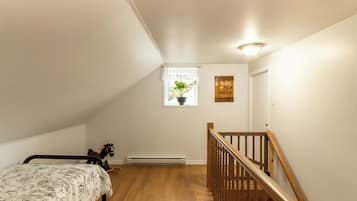A bedroom with a bed, a window with a plant, a wooden staircase, and a wall with a sign.