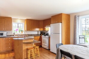 Una cocina compacta con armarios de madera, una isla central con taburetes, un refrigerador y una ventana con vistas.