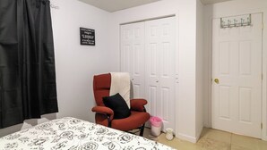 Un dormitorio con una cama, una silla roja, una puerta blanca y un letrero negro en la pared.