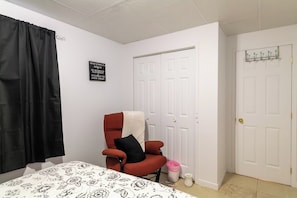 A bedroom with a bed, a red chair, a white door, and a black sign on the wall.