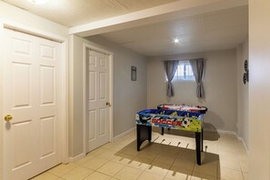 Un pasillo con una mesa de fútbol de mesa, una puerta y una ventana con cortinas.