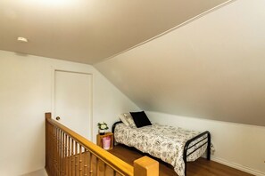 A small, single-bed room with a sloped ceiling, a wooden staircase, and a white door.