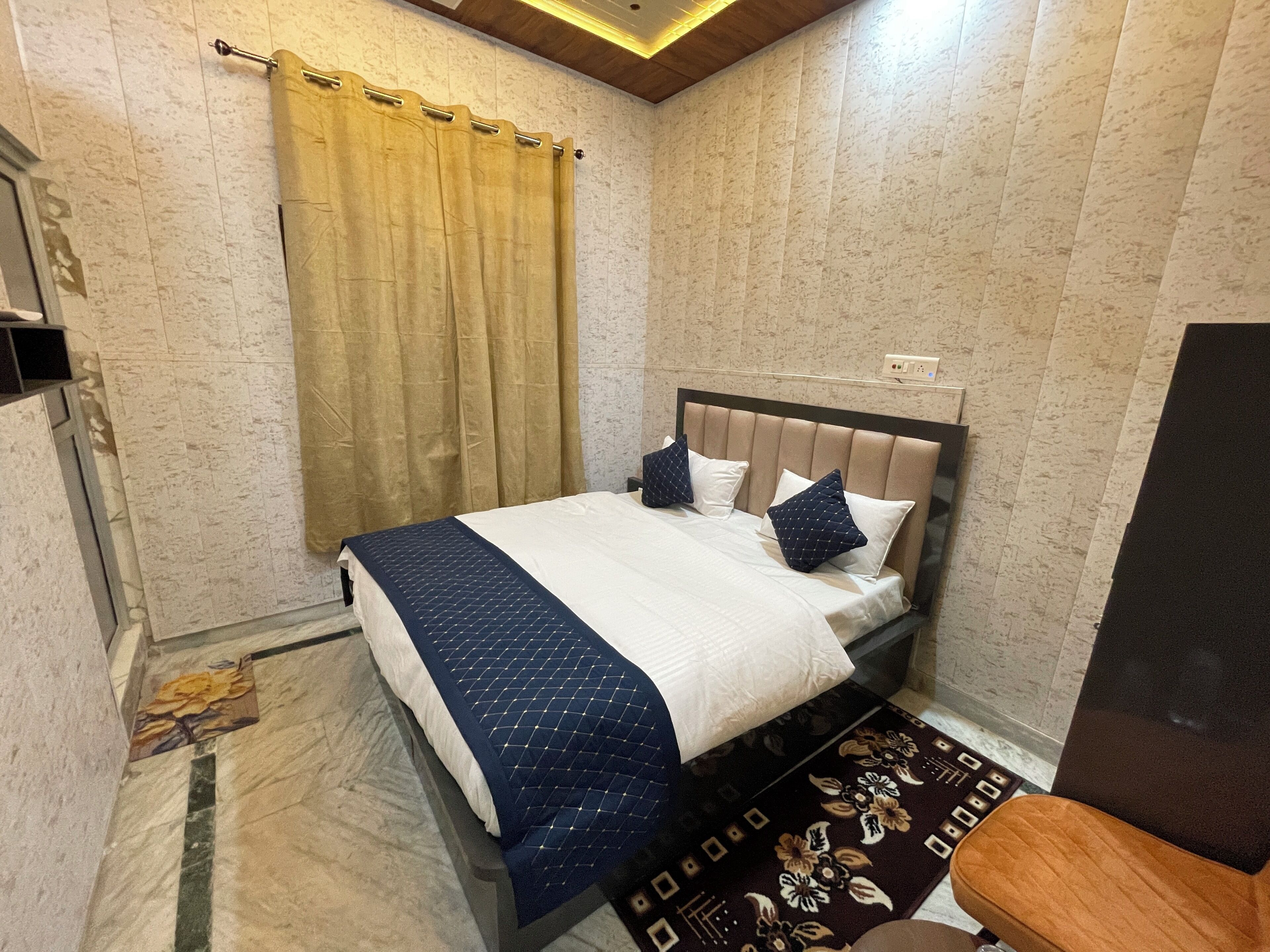 A neatly made bed with a headboard, a wooden chair, and a patterned rug.