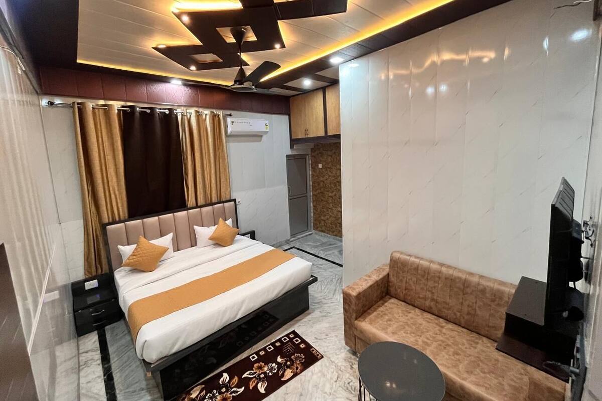 A modern hotel room with a large bed, a sofa, a TV, and a ceiling fan.