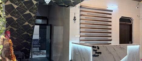 Una moderna zona de recepción con mostrador de mármol, pared con motivo geométrico y una lámpara de araña.