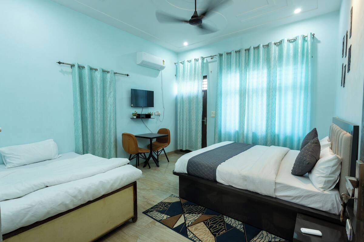 A hotel room with two beds, a desk, a chair, a TV, and a ceiling fan.