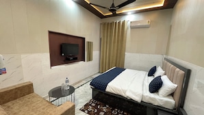 Quarto de hotel com cama, televisão na parede, ventilador de teto e uma mesinha com garrafa e copos.