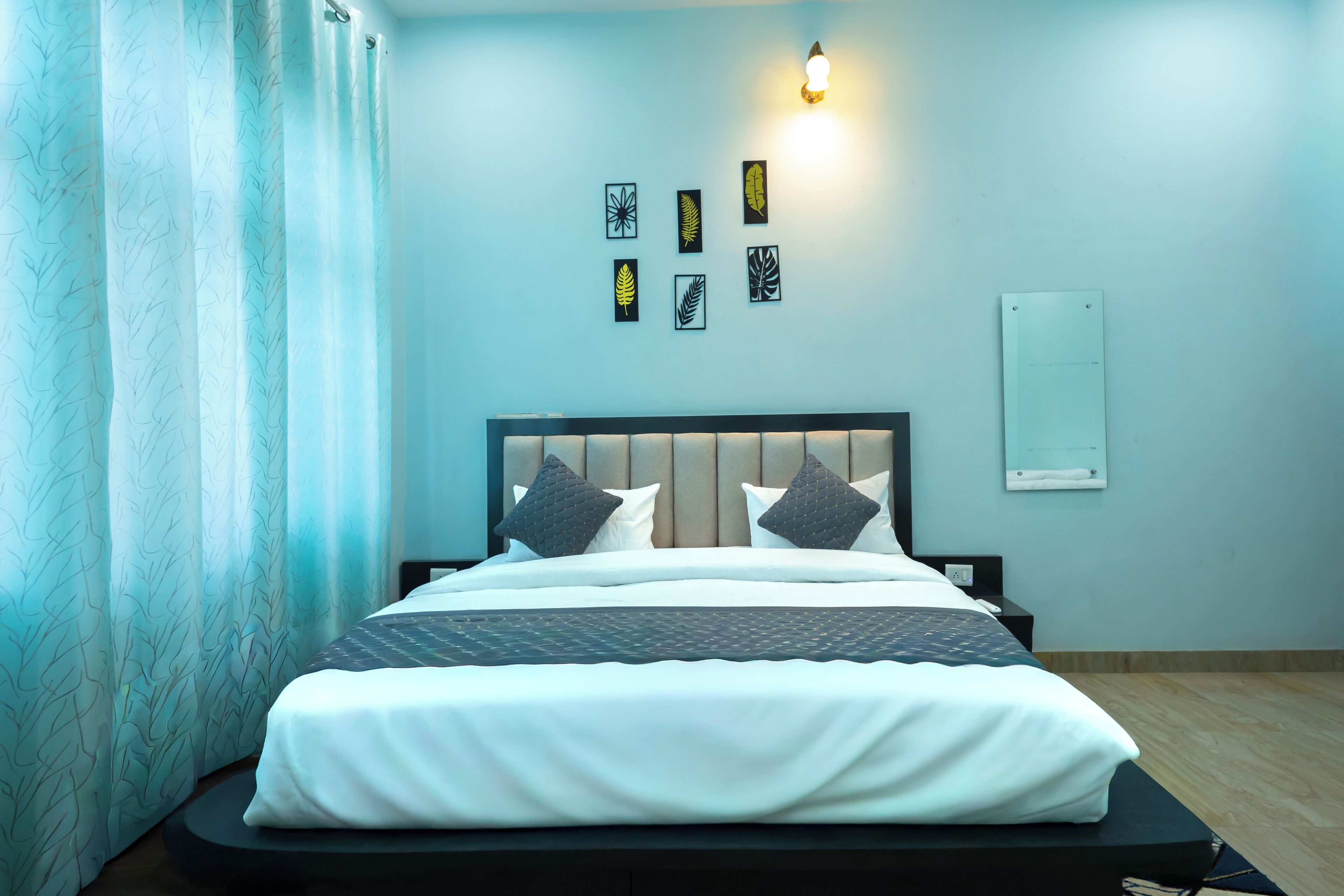 A neatly made bed with a headboard, a wall-mounted light fixture, and four framed leaf designs.