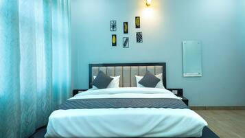 Een net opgemaakt bed met hoofdbord, een wandlamp en vier ingelijste bladmotieven.