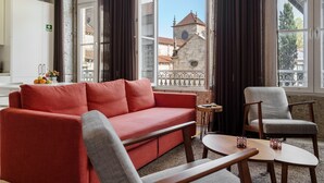 A modern living room with a red sofa, grey armchair, and wooden coffee table. Large windows offer a view of a historic building. - Bracara Home By Minhos Guest (Braga)