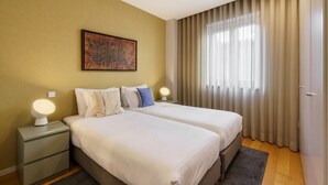A hotel room with two beds, a nightstand with a lamp, a painting on the wall, and a window with curtains. - Bracara Home By Minhos Guest (Braga)