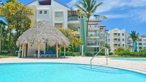 Un hôtel doté d’une piscine, d’une structure au toit de chaume et d’un palmier.