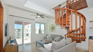 Ein Wohnzimmer mit einer Wendeltreppe aus Holz, einem Sofa, einem Couchtisch und einem Fernseher auf einem Holzgestell.