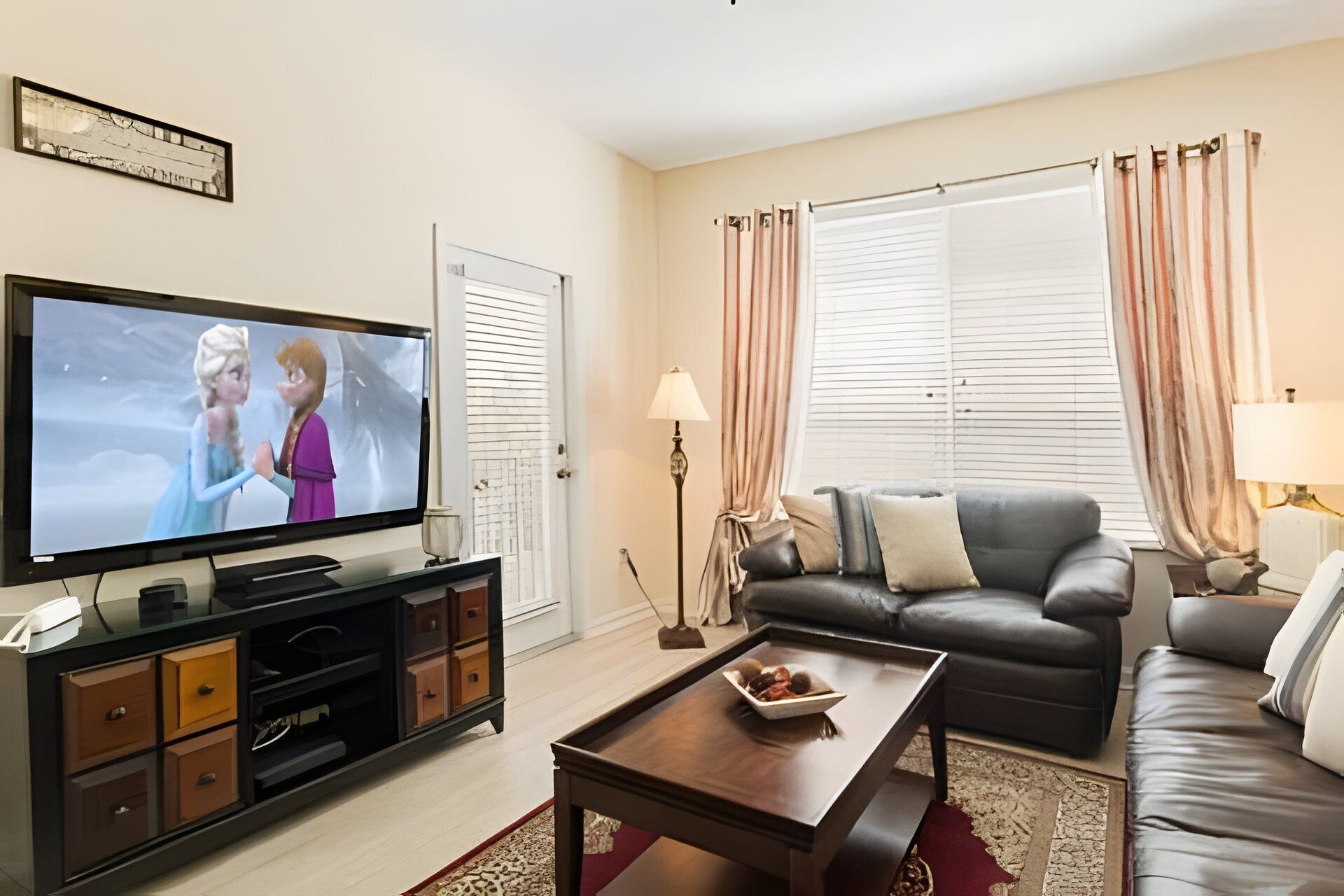 A living room with a flat-screen TV, a black leather sofa, a wooden coffee table, and a patterned rug.