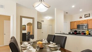 Ein Esszimmer mit gedecktem Tisch für vier Personen, im Hintergrund eine Küche und ein Flur, der in ein weiteres Zimmer führt.