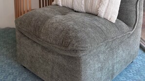 Un coin salon accueillant avec un canapé gris, un coussin en tricot blanc, une petite table d'appoint en bois sur laquelle sont posés un vase blanc et une plante, et un grand lampadaire à abat-jour blanc.